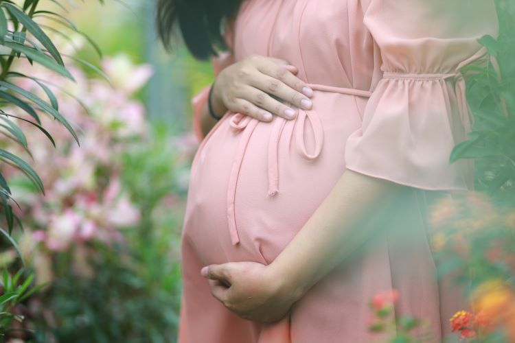 Kobieta w ciąży w różowej sukience na tle roślinności – Hipnoterapia